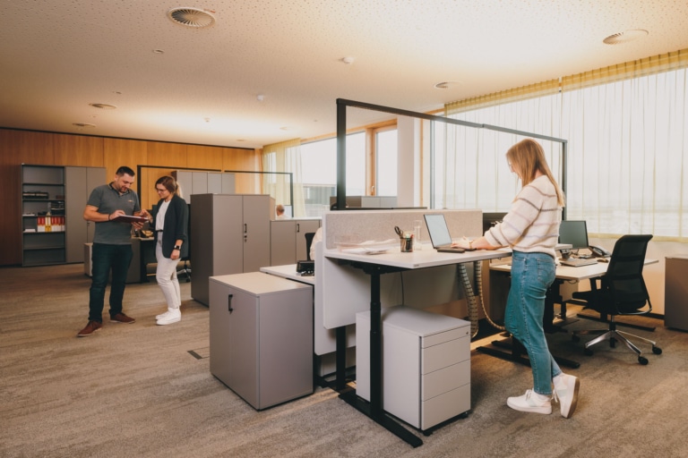Drei Personen in einem modernen Büro mit höhenverstellbaren Schreibtischen - moderner Arbeitsplatz